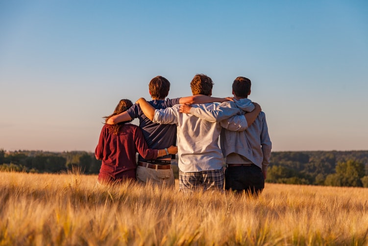 four teenage friends standing in a field looking away into the distance, with arms around each other, showing that kids will feel more secure when there is parental involvement in the home.
