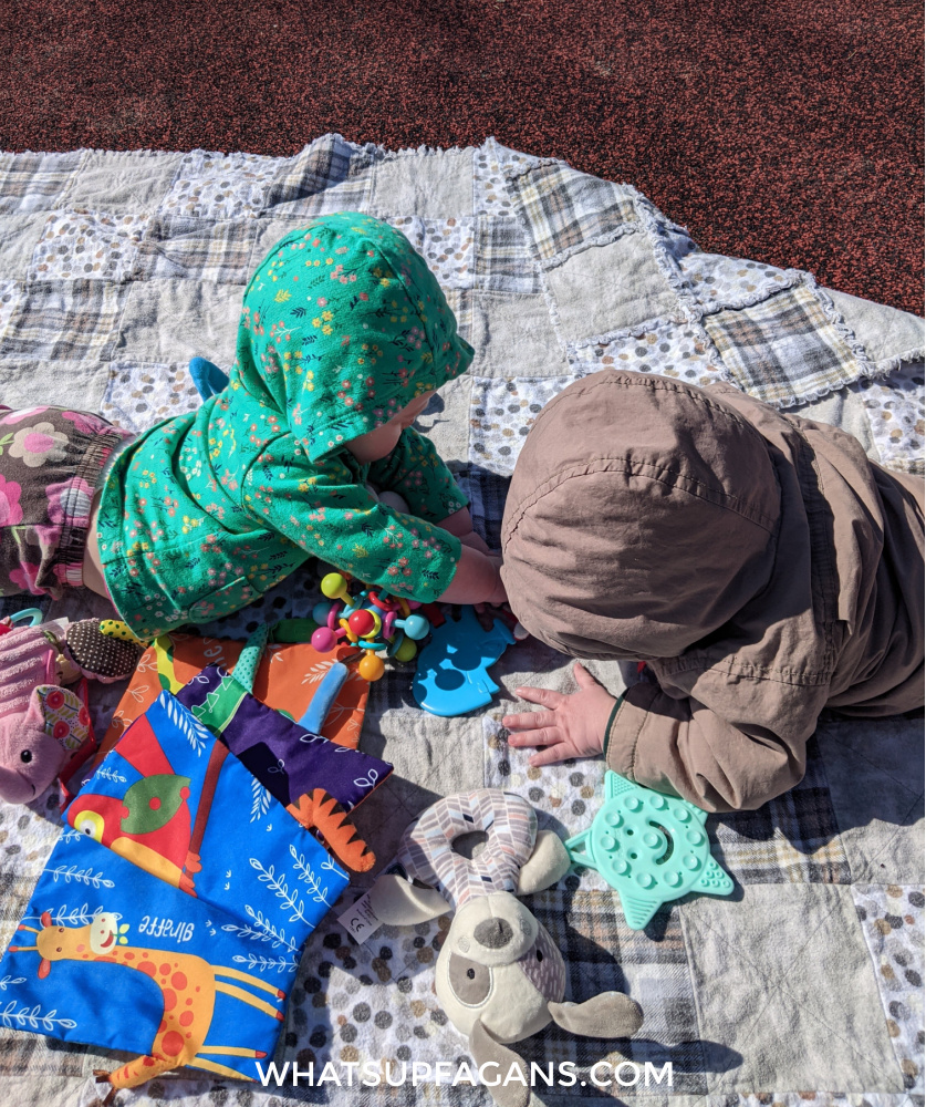 twin babies crawling on a blanket with toys outside as a means to discuss outdoor safety for babies