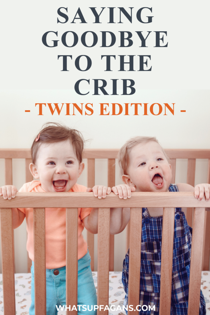 Cute fraternal twin girls standing up in a crib, wondering when to move from crib to a toddler bed for tinws.